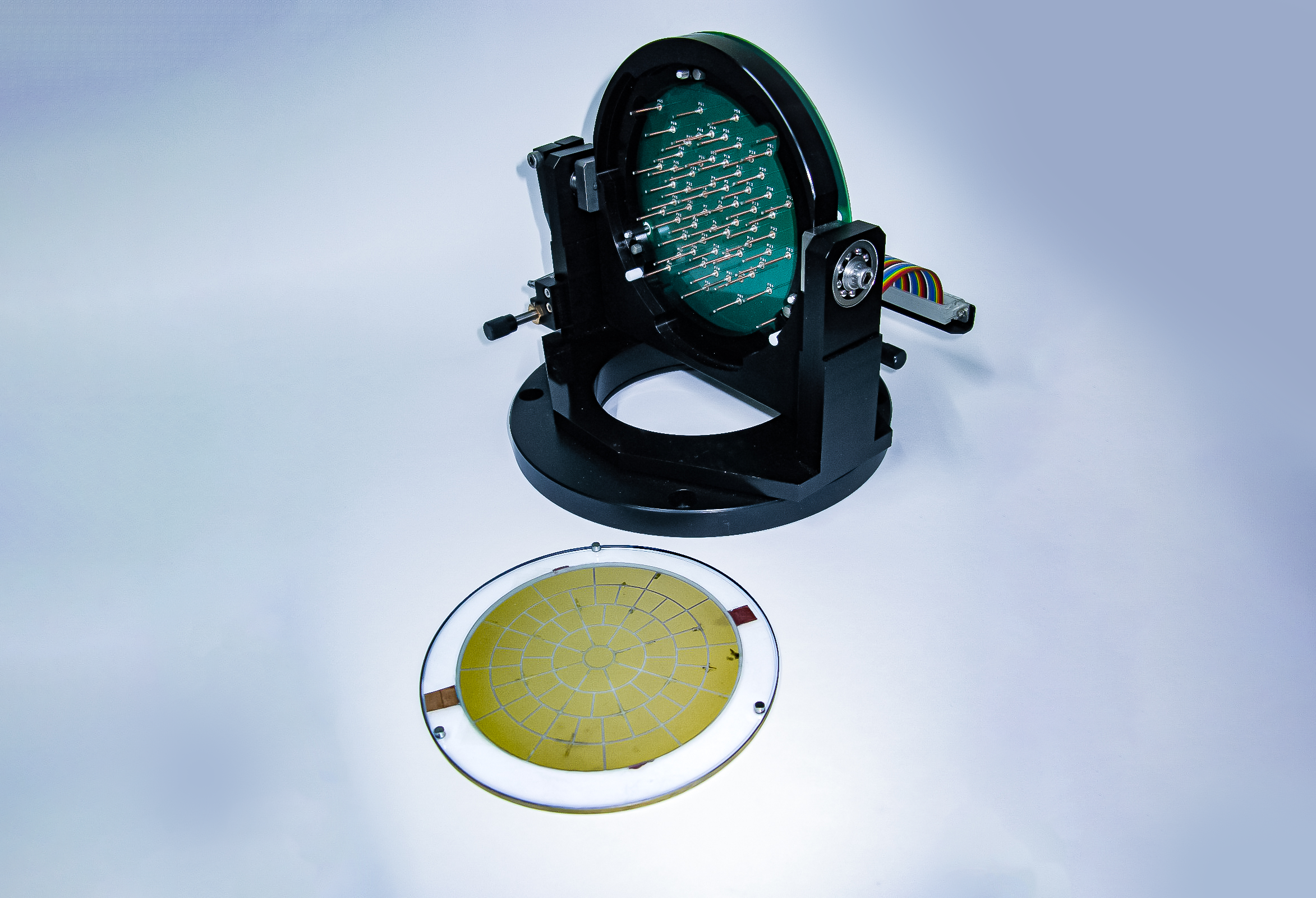 A circular optic in a black mount. The optic has protruding from its surface multiple tiny spike-like metal objects in a uniform, ringed fashion.